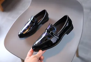 Détail de mocassins noirs pour garçons en cuir verni avec texture camouflage et boucle