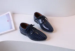 Détail de chaussures en cuir bleu pour garçon avec motif crocodile sur présentoir blanc