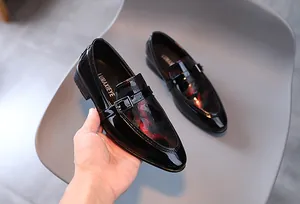 Détail d'une chaussure en cuir verni noir pour garçon avec boucle et texture rouge