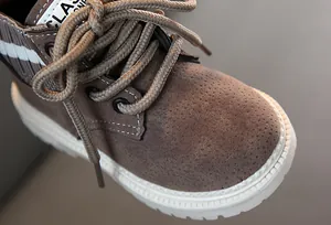 Nahaufnahme brauner Wildleder-Kinderstiefel mit geflochtenen Schnürsenkeln und weißer Sohle