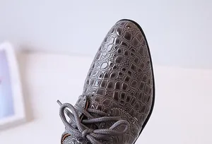 Macro detail of boys grey crocodile embossed patent leather shoes with lace-up design