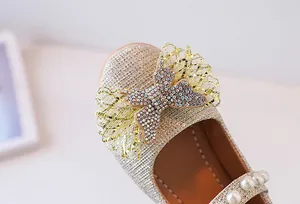 Primer plano de zapatos Mary Jane dorados con purpurina, lazo de diamantes y detalle de perla