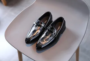 Détail de mocassins noirs vernis pour garçons avec texture diamant et boucle argentée
