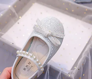 Detail of glitter girl Mary Jane shoes with pearl strap and elegant bow decoration