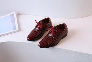 Détail de chaussures habillées pour garçons en cuir bordeaux embossé crocodile lacé