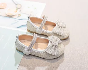 Dettaglio di scarpe Mary Jane dorate da bambina con glitter, fiocco e cinturino di perle