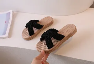 Close-up of women's flat slides with beige woven straw texture and black pleated cross straps
