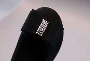 Détail d'une chaussure noire en daim pour fille avec un nœud décoratif en strass brillants