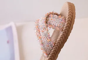 Dettaglio dei cinturini dei sandali beige con fili rosa, arancioni e argento glitter