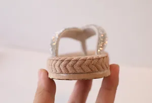 Detailed close-up of champagne flip flops featuring glittery straps and woven texture sole