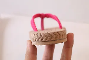 Detailed side view of thick-soled flip-flops with pink braided strap and straw-like texture