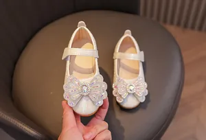 Detail of white girls' Mary Janes featuring sparkling rhinestone bows and velcro straps