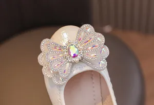 Close-up of a glossy cream girls' princess shoe featuring a rhinestone bow and colorful gem