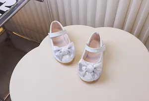 Detail van witte lakschoenen Mary Jane met een sprankelende zilveren strik erop