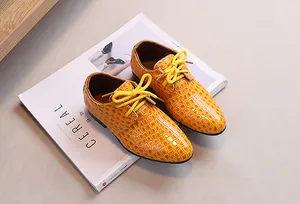 Top-down view of boys' yellow crocodile embossed leather derby shoes on cereal magazine