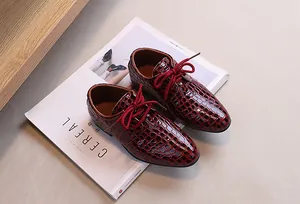 Close-up of burgundy boy's leather shoes with embossed crocodile texture and red laces