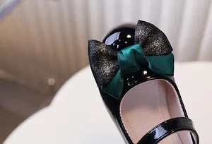 Detail van zwarte lakschoenen voor meisjes met een vintage satijnen strik en goudglitter
