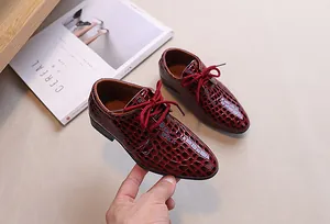 Detailed view of dark burgundy crocodile-embossed patent leather shoes for boys