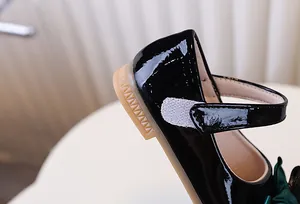 Detail van zwarte lakschoenen voor meisjes met een groene satijnen strik en klittenband