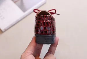 Detail of dark red faux crocodile leather boy's shoe with a decorative rear bow tie