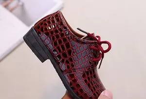 Detail of burgundy crocodile-embossed patent leather boy dress shoes with lace-up finish