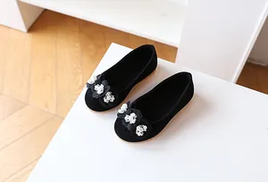 Detail of girls' black suede flats featuring delicate 3D flowers and pearl embellishments