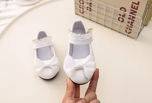 Close-up of white patent leather Mary Jane shoes with organza bow and lace trim