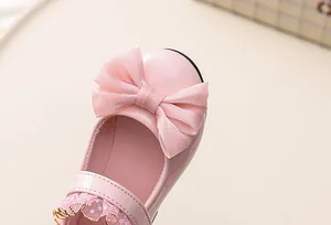 Close-up of pink patent leather girl shoes with tulle bow and gold edge lace detail