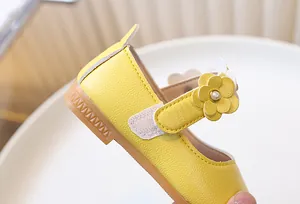 Detailed view of yellow Mary Jane shoe featuring floral leather trim and pearl center