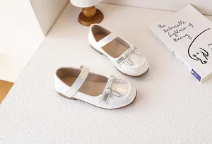 Dettaglio scarpe Mary Jane bianche con fiocco di perle e strass su scrivania