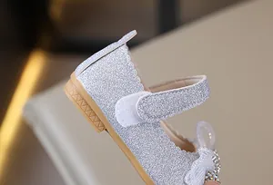 Detalle de zapatos plateados con purpurina para niñas con lazo de strass y borde