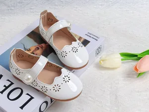 Détail de babies en cuir verni blanc avec découpes de fleurs et bouton perle