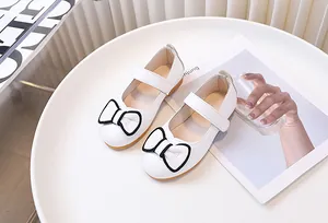 Dettaglio scarpe Mary Jane bianche con fiocchi a bordo nero e cinturini in velcro