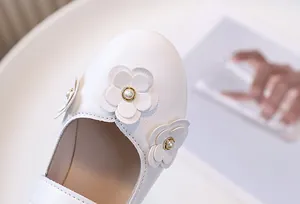 Detalle de zapatos de princesa blancos para niña con flores 3D y perlas centrales