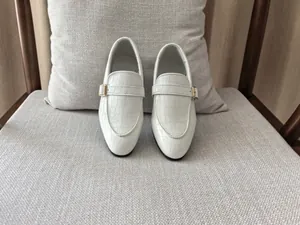 Detailed view of white crocodile texture leather loafers with a golden metal buckle