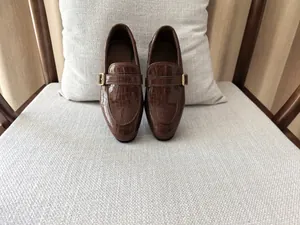 Detail of brown crocodile pattern leather loafers with decorative gold buckles