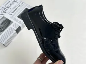 Detail of boys' black patent leather oxford shoes with textured side panels and laces