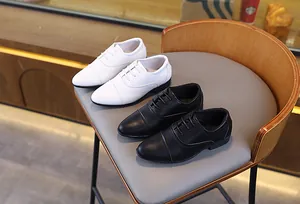 Gros plan de chaussures habillées pour garçons en cuir noir et blanc sur une chaise