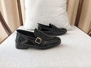 Detail of boys' black faux crocodile leather loafers featuring a golden metal buckle