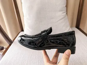 Macro shot of black crocodile embossed patent leather kids loafers showing material texture