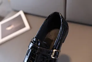 Dettaglio scarpe in pelle nera a motivo coccodrillo con fibbia in metallo dorato