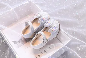 Détail de chaussure Mary Jane argentée à paillettes avec nœud en dentelle et strass