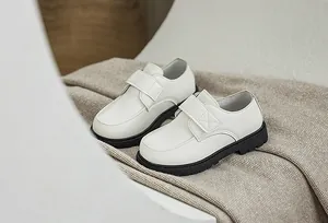 Close-up of white leather kids' dress shoes featuring hook and loop straps and thick soles