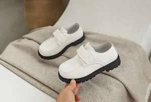 Detail of white boys' leather shoe featuring a velcro strap and thick black rubber sole