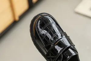 Detailed macro view of black patent leather boys shoes with crocodile embossed pattern