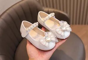 Dettaglio di scarpe da principessa bianche per bambina con fiocco in pizzo e perla