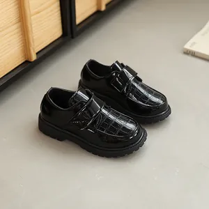 Classic black boys loafers with crocodile pattern and velcro strap on gray floor