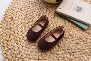 Close-up of girls' burgundy velvet Mary Jane flat shoes with elastic strap on a woven mat