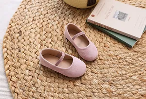 Top view of pink suede girls' Mary Jane shoes with elastic strap on a natural woven mat