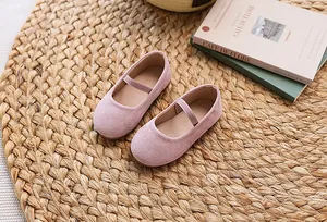 Detail of pink suede Mary Jane flat for girls with elastic strap on a straw mat